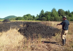 a man stands pointing to a pile of biosolids on a farm